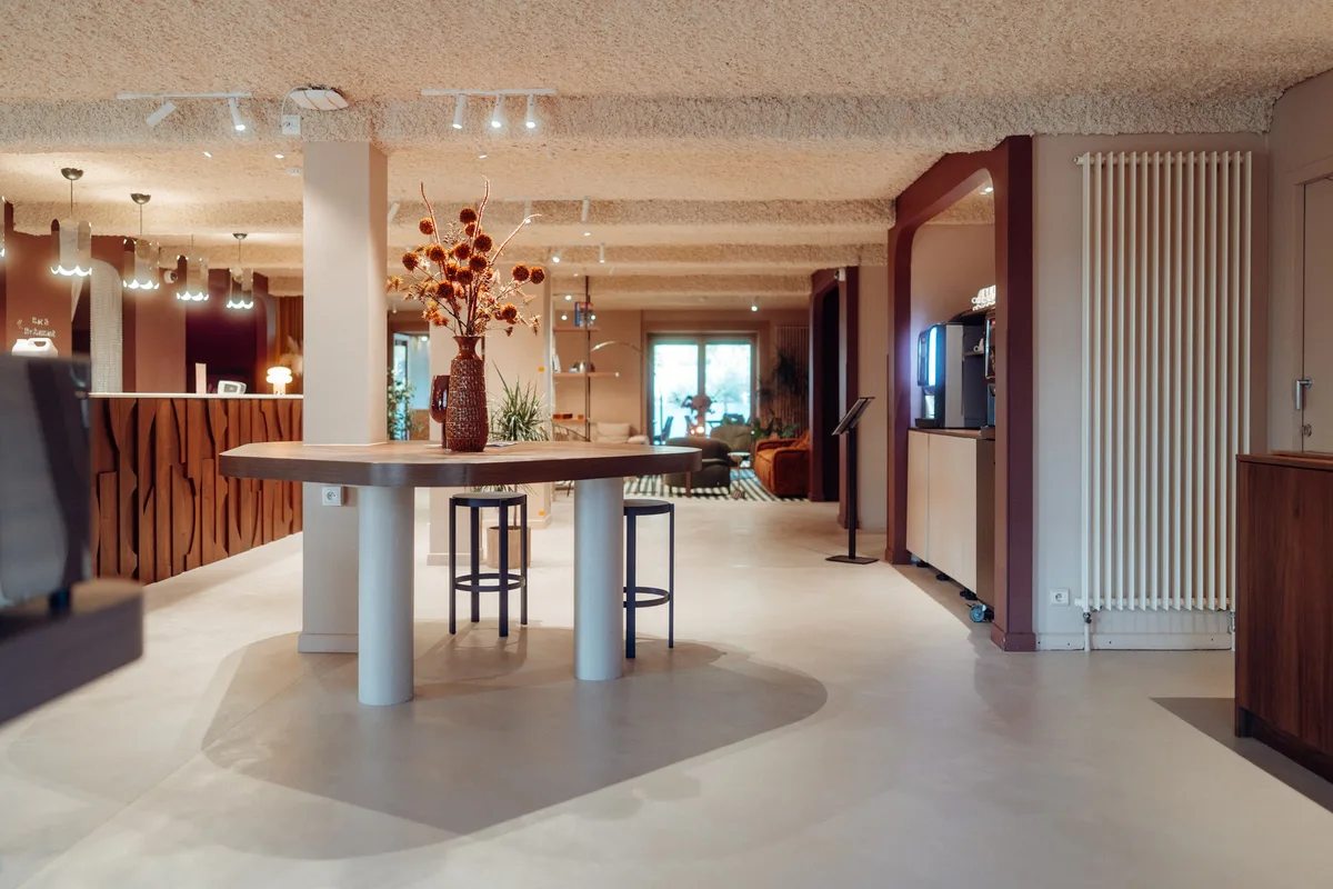 Hall et bar de la Maison Melba à Bastogne : béton ciré clair et zone courbe plus foncée sous la table haute