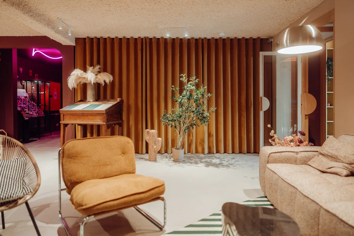 Coin salon de la Maison Melba avec fauteuil orange et canapé, sol en béton ciré clair