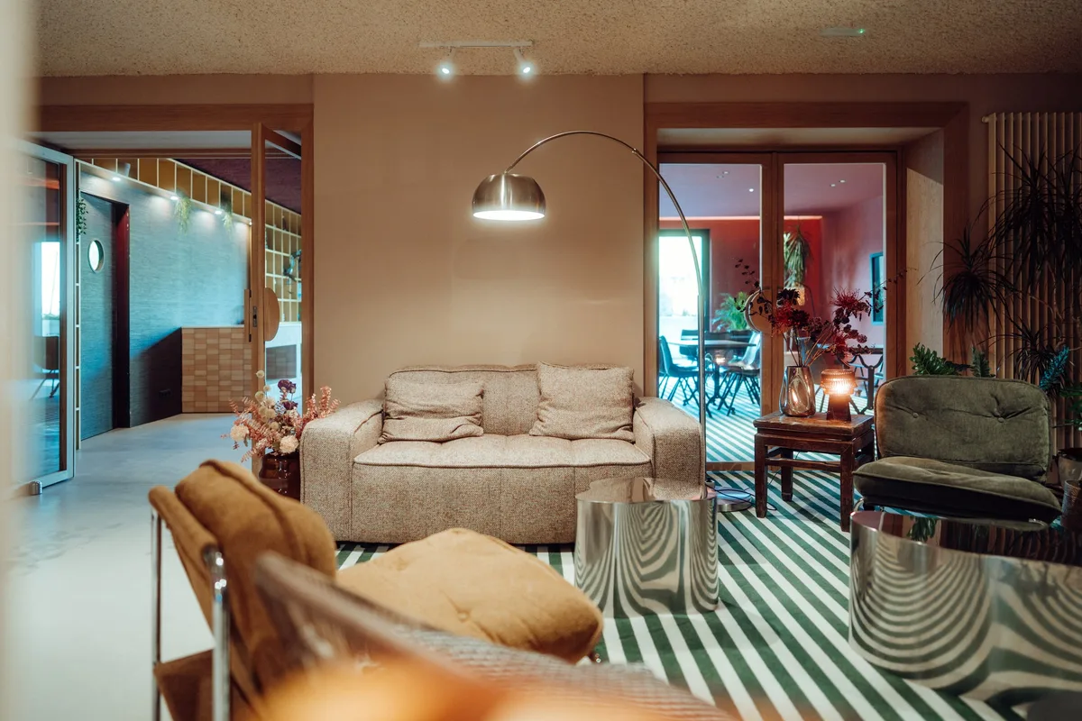 Salon de la Maison Melba avec canapé, fauteuils et moquette rayée, sol en béton ciré
