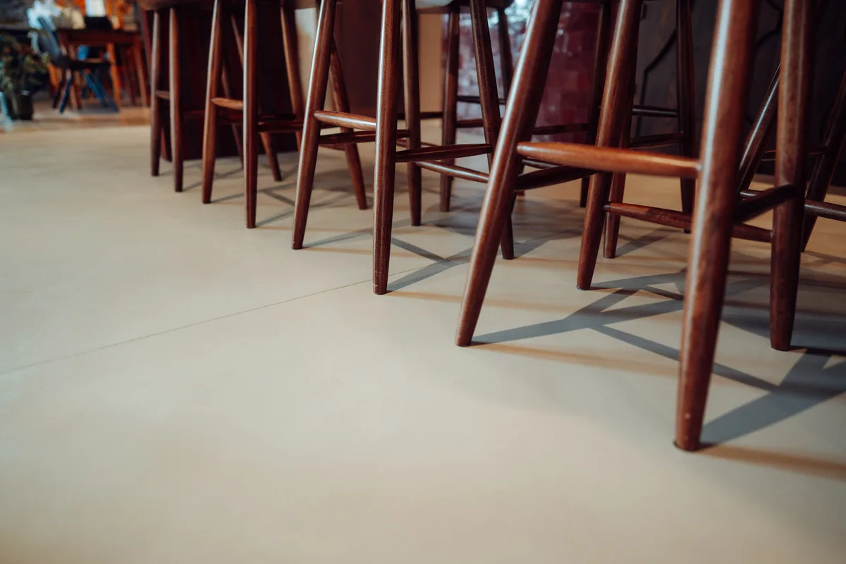 Pieds de tabourets en bois sur le béton ciré lisse du bar de la Maison Melba