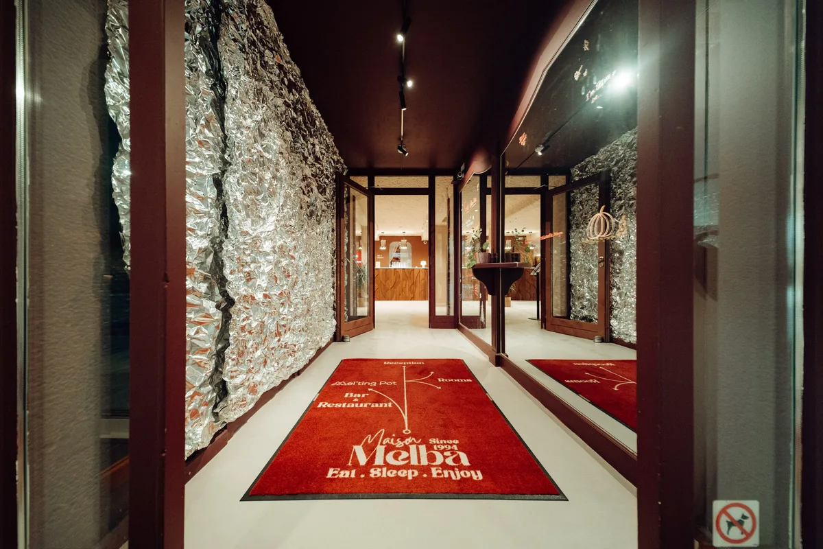 Couloir d’entrée de la Maison Melba avec tapis rouge au logo, sol en béton ciré clair