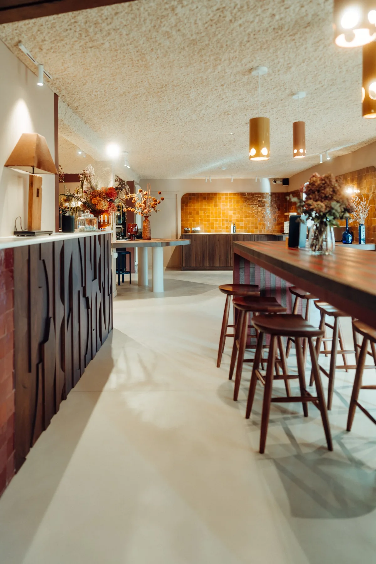 Bar en bois sculpté, tabourets et coin café de la Maison Melba, sol en béton ciré