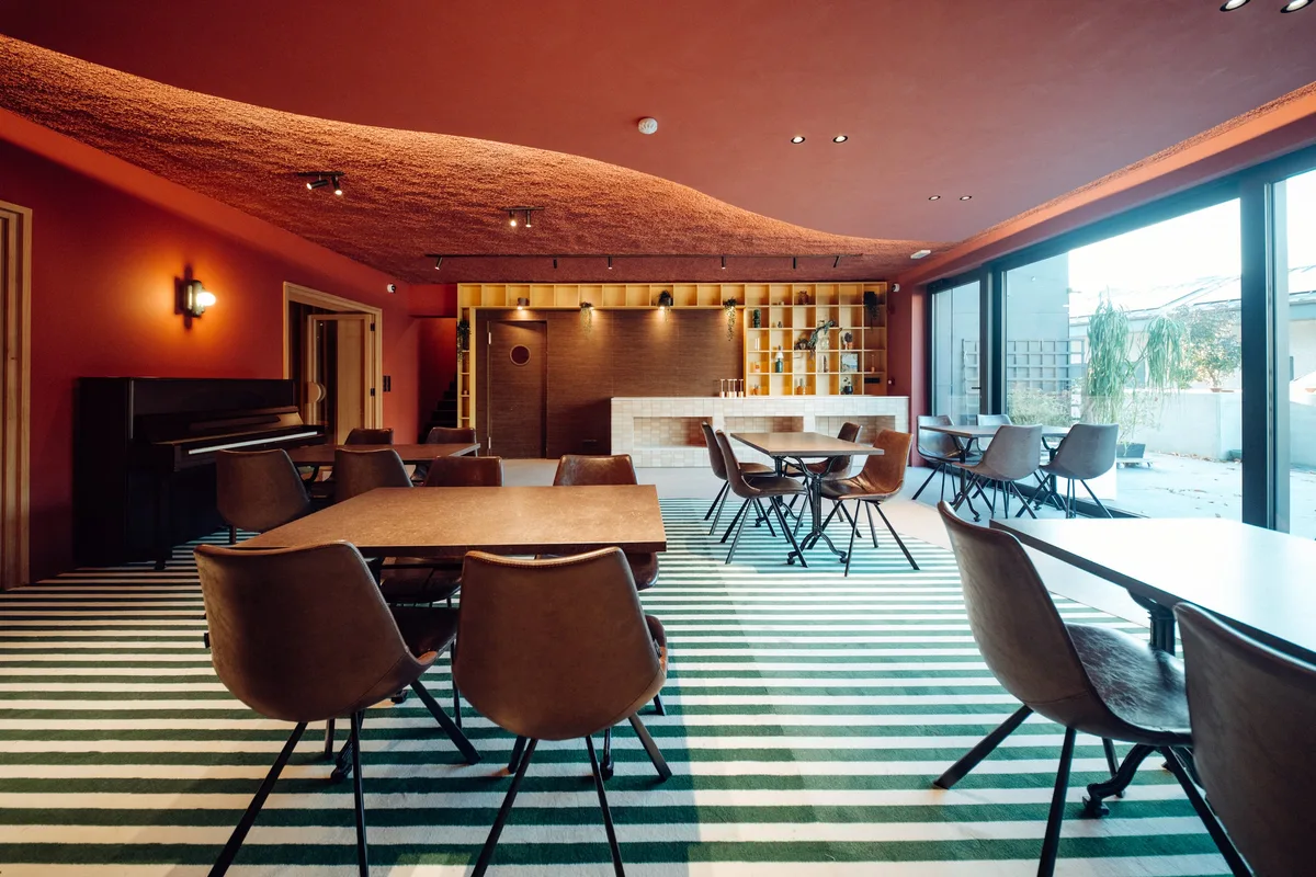 Salle de restaurant de la Maison Melba avec moquette rayée vert et blanc, tables en bois et chaises en cuir